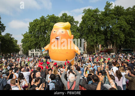 London, Großbritannien. 13. Juli 2018. Anti-Trump Aktivisten heben Trump Baby, ein 6 Meter hoher Helium - Schlauchboot gefüllt mit Donald Trump als orange - behaarte Baby in Windeln, über Parliament Square aus Protest gegen den Besuch von Präsident Trumpf. Wurde die Erlaubnis für den Protest aufblasbare durch den Bürgermeister von London Sadiq Khan gegeben. Credit: Mark Kerrison/Alamy leben Nachrichten Stockfoto