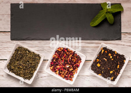 Von oben, verschiedene Arten von trockenen Kaffee in kleinen quadratischen Platten und schwarzem Schiefer Board auf weißem Holz- Hintergrund Stockfoto