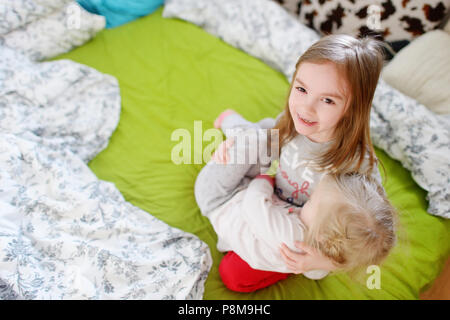 Zwei kleine Schwestern durchgeklickt, spielen und Spaß haben im Bett an sonnigen Sonntag Morgen Stockfoto