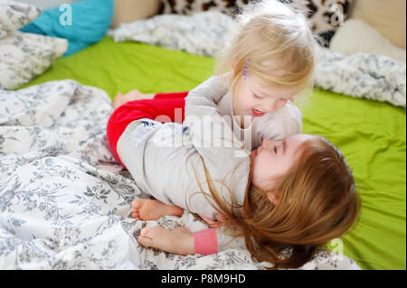 Zwei kleine Schwestern durchgeklickt, spielen und Spaß haben im Bett an sonnigen Sonntag Morgen Stockfoto