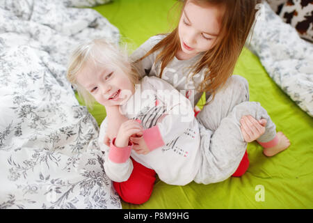 Zwei kleine Schwestern durchgeklickt, spielen und Spaß haben im Bett an sonnigen Sonntag Morgen Stockfoto