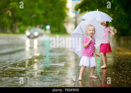 Zwei süße kleine Schwestern in einer Pfütze holding Dach stehend auf einem verregneten Sommertag Stockfoto