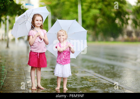 Zwei süße kleine Schwestern in einer Pfütze holding Dach stehend auf einem verregneten Sommertag Stockfoto