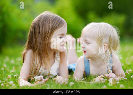 Zwei süße kleine Schwestern Spaß beim mit in das Gras an einem sonnigen Sommertag Stockfoto