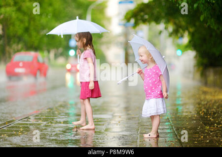 Zwei süße kleine Schwestern in einer Pfütze holding Dach stehend auf einem verregneten Sommertag Stockfoto