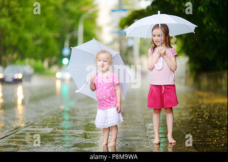 Zwei süße kleine Schwestern in einer Pfütze holding Dach stehend auf einem verregneten Sommertag Stockfoto