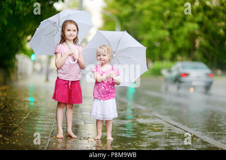 Zwei süße kleine Schwestern in einer Pfütze holding Dach stehend auf einem verregneten Sommertag Stockfoto