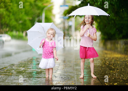 Zwei süße kleine Schwestern in einer Pfütze holding Dach stehend auf einem verregneten Sommertag Stockfoto