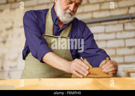 Bärtigen Handwerkers mit dem grauen Haar ist bei der Arbeit mit Bohlen gut. Nahaufnahme 7/8 Hochformat Stockfoto