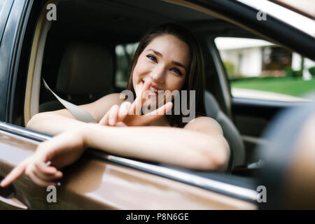 Lächelnde junge Frau tut Frieden Zeichen im Auto Stockfoto