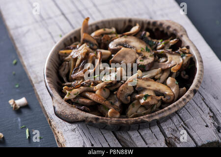 Nahaufnahme einer braunen Steingut Schale mit einige gekochte gemischte Pilze, wie z. B. gemeinsame Champignons, Austernpilze und Shiitake, auf einem weißen Holzmöbeln im Landhausstil Stockfoto