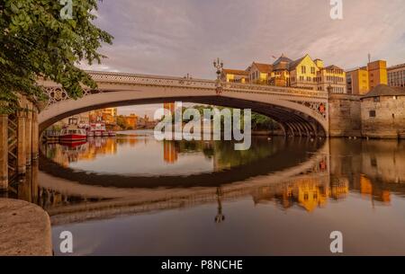 Ein Blick auf den Fluss Ouse Richtung Lendal Bridge und die Skyline der Stadt. Tour boote Linie der linken Ufer mit Bäumen auf beiden Seiten. Die Brücke ist Spiegeln Stockfoto