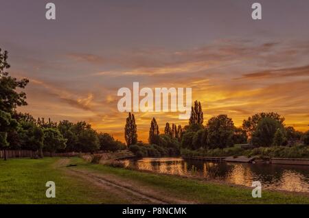 Ein dramatischer Sonnenuntergang über einem Bogen in den Fluss Ouse in York. Ein Pfad führt entlang einer von Bäumen gesäumten Ufer. Stockfoto