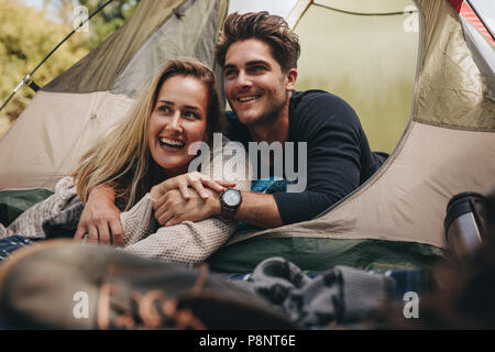 Attraktive Paare in ihrem Zelt liegend weg schauen und lächeln. Liebevolle junge Paar entspannende im Zelt. Stockfoto