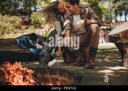 Romantisches Paar von Lagerfeuer sitzen und Marshmallows rösten in Brand. Schönes Paar in der Liebe genießen, auf einem Campingplatz. Stockfoto