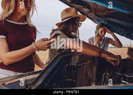 Frau, die versucht, das Auto mit Freunden telefonieren, um Hilfe zu beheben. Frau, die versucht, das Auto auf der Autobahn einen Road Trip mit Freunden zu reparieren. Stockfoto