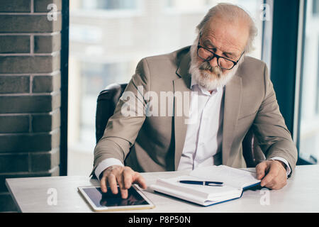 Nahaufnahme Foto von Stattlichen grauhaarige ältere Unternehmer arbeiten mit Tablet in der Loft Büro Stockfoto