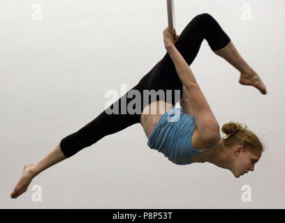 Eine weibliche Acrobat schaukeln auf den Kopf von einer Antenne Hoop. Stockfoto