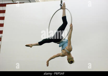 Eine weibliche Acrobat schaukeln auf den Kopf von einer Antenne Hoop. Stockfoto