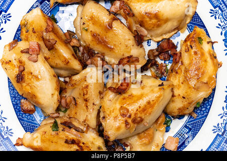 Wareniki, vareniki, Pierogi, pyrohy oder Knödel, mit Käse und Kartoffeln gefüllt, serviert mit Zwiebel und Speck auf einem blauen Platte Stockfoto