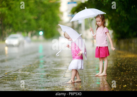 Zwei süße kleine Schwestern in einer Pfütze holding Dach stehend auf einem verregneten Sommertag Stockfoto