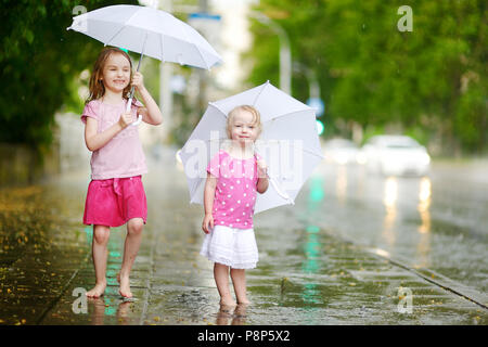 Zwei süße kleine Schwestern in einer Pfütze holding Dach stehend auf einem verregneten Sommertag Stockfoto