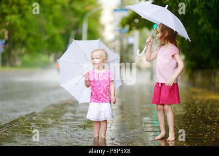 Zwei süße kleine Schwestern in einer Pfütze holding Dach stehend auf einem verregneten Sommertag Stockfoto