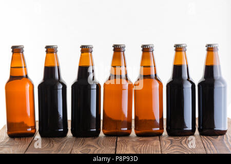 Reihe von Dunkelheit und Licht nicht etikettierten Flaschen mit hausgemachten Handwerk Bier auf einem rustikalen Holztisch vor einem weißen Hintergrund Stockfoto