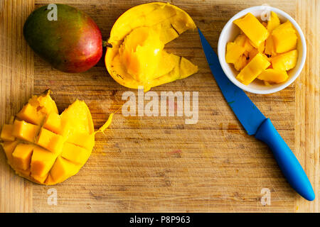 In Scheiben geschnittene reife Mango in eine Schüssel und Igel Form auf einem Bambus Schneidebrett mit bunten blauen Küchenmesser und Platz kopieren Stockfoto