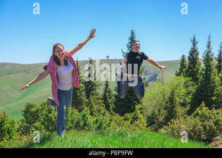 Eine glückliche Paare. Frau in einem rosa Weste und Blue Jeans ihre Arme und springt auf einem Fuß. Ein Mann mit einem Smiley springt auf beiden Füßen Stockfoto
