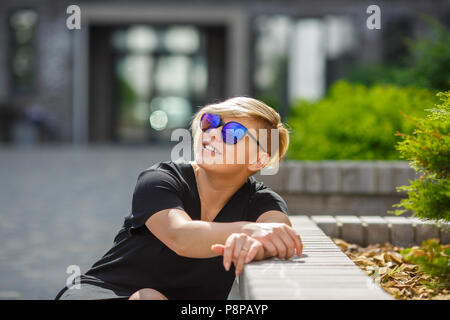 Das Mädchen plus die Größe in Sonnenbrille, Lächeln, Freude, an einem sonnigen Tag auf der Straße fröhlich, ein Haarschnitt ist kreativ. Die Teilnehmer bestanden die Prüfungen, e Stockfoto