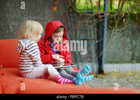 Zwei Entzückende kleine Schwestern spielen mit einem digitalen Tablet im Freien auf Herbst Tag Stockfoto