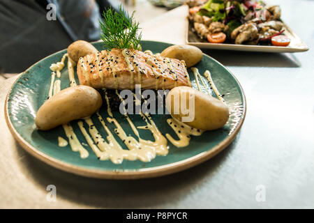 Gegrillter Lachs auf einer Platte mit einem schwarzen Bulgur und mit gekochten Kartoffeln für ein Abendessen arrangiert platziert Stockfoto