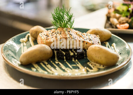 Gegrillter Lachs auf einer Platte mit einem schwarzen Bulgur und mit gekochten Kartoffeln für ein Abendessen arrangiert platziert Stockfoto