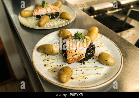 Gegrillter Lachs auf einer Platte mit einem schwarzen Bulgur und mit gekochten Kartoffeln für ein Abendessen arrangiert platziert Stockfoto