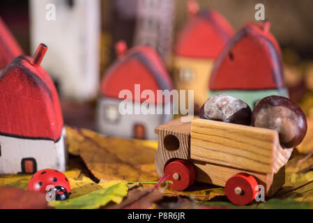 Spielplatz für Kinder, Anordnung von bemalten Spielzeug Holzhäuser, Lkw mit Kastanien, Marienkäfer auf der Blätter im Herbst. Kindheit Konzept Stockfoto