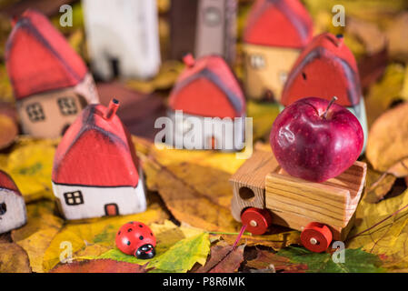 Spielplatz für Kinder, Anordnung von bemalten Spielzeug Holzhäuser, Lkw mit einem Apple, Marienkäfer auf der Blätter im Herbst. Kindheit Konzept Stockfoto