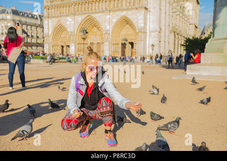 Glückliche junge touristische Frau füttert Tauben in Notre Dame entfernt. Kaukasische lifestyle Reisenden genießt in Paris, Frankreich, Europa. Beliebtes Touristenziel in der französischen Hauptstadt. Stockfoto