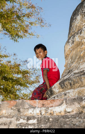 Bagan, Myanmar, 29. Dezember 2017: lächelnde Junge mit Tanaka im Gesicht sitzt am Fuße eines Stupa in Bagan, Myanmar Stockfoto