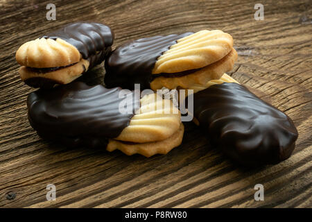 Cookies auf Holztisch. Kekse mit Füllung auf Holzschreibtisch. Süße Cookies in Schokolade getauchten. Stockfoto