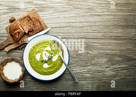 Frische, gesunde grüne Suppe mit Sahne auf hölzernen Hintergrund serviert. Stockfoto