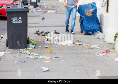 Person zu Fuß vorbei an einem Wurf übersäte Straße mit Tauben Ernte an den Müll auf dem Boden liegend in Hastings, East Sussex, Großbritannien Stockfoto