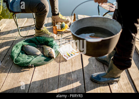 Zwei Fischer bereitet etwas zu Essen während der Picknick auf der hölzernen Pier in der Nähe des Sees am Morgen Stockfoto