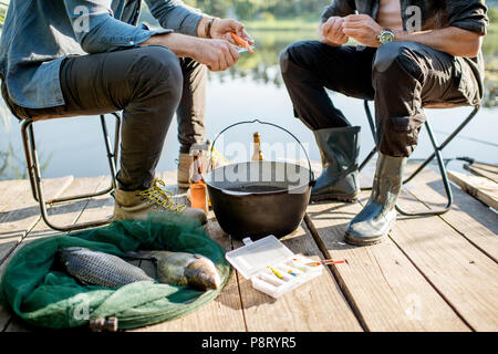 Zwei Fischer bereitet etwas zu Essen während der Picknick auf der hölzernen Pier in der Nähe des Sees am Morgen Stockfoto