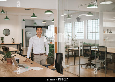 Junge asiatische Geschäftsmann, Lächeln, während er durch sein Büro Schreibtisch Stockfoto