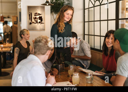 Lächelnde Kellnerin, die Aufträge von Kunden in einem Bistro Stockfoto