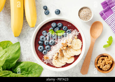 Acai smoothie Schüssel mit Blaubeere, Banane, Nussbaum, Kokos und Chia Samen auf hellen konkreten Hintergrund, Ansicht von oben. Gesunde Lebensweise, gesunde eati Stockfoto