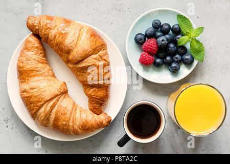 Croissant, schwarzen Kaffee, Orangensaft und frische Beeren Heidelbeeren Himbeeren auf konkreten Hintergrund. Ansicht von oben. Frühstück, Brunch, Kaffee oder Snack Stockfoto