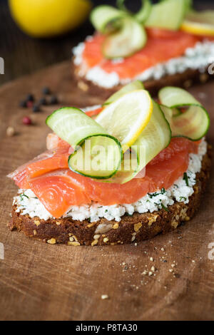 Lecker geräucherten Lachs Sandwich mit Frischkäse, Gurken und Scheibe Zitrone auf Holzbrett, Detailansicht, selektiver Fokus Stockfoto