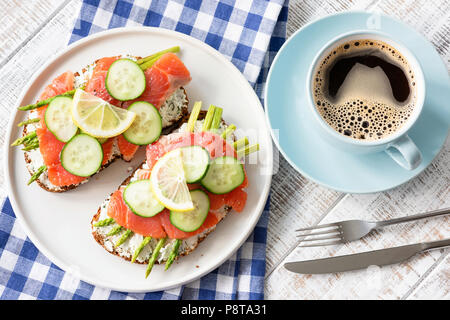 Frühstück Sandwiches mit Lachs, Spargel, Frischkäse und Tasse Kaffee auf weiße Holztisch. Ansicht von oben. Gesundes Frühstück, Kaffeepause Stockfoto